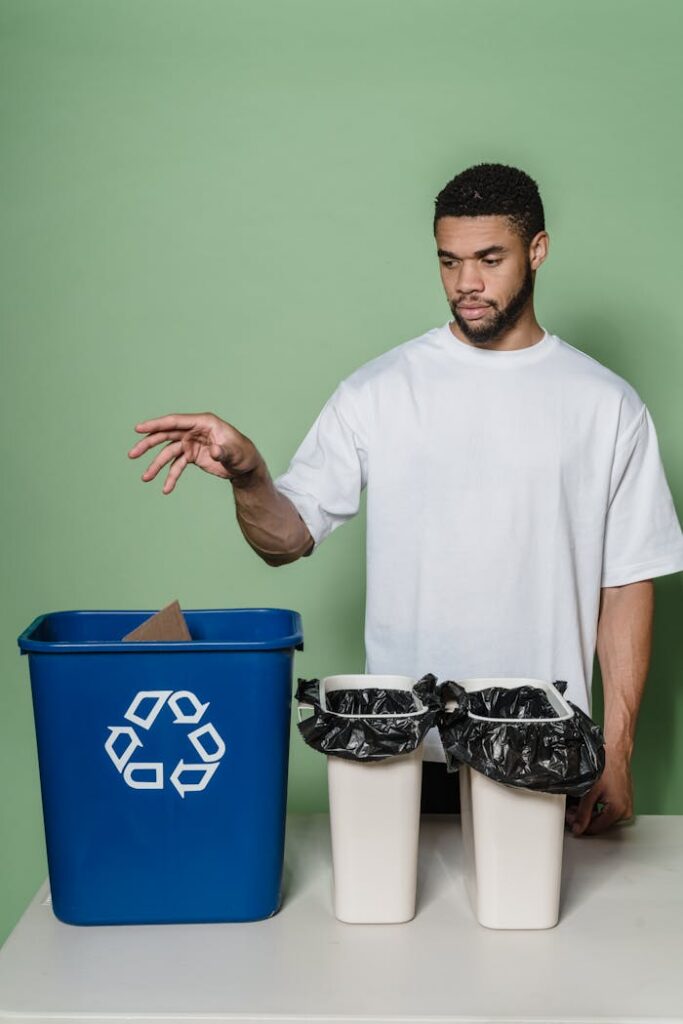 Man in white shirt recycling in studio with blue bin and green background.